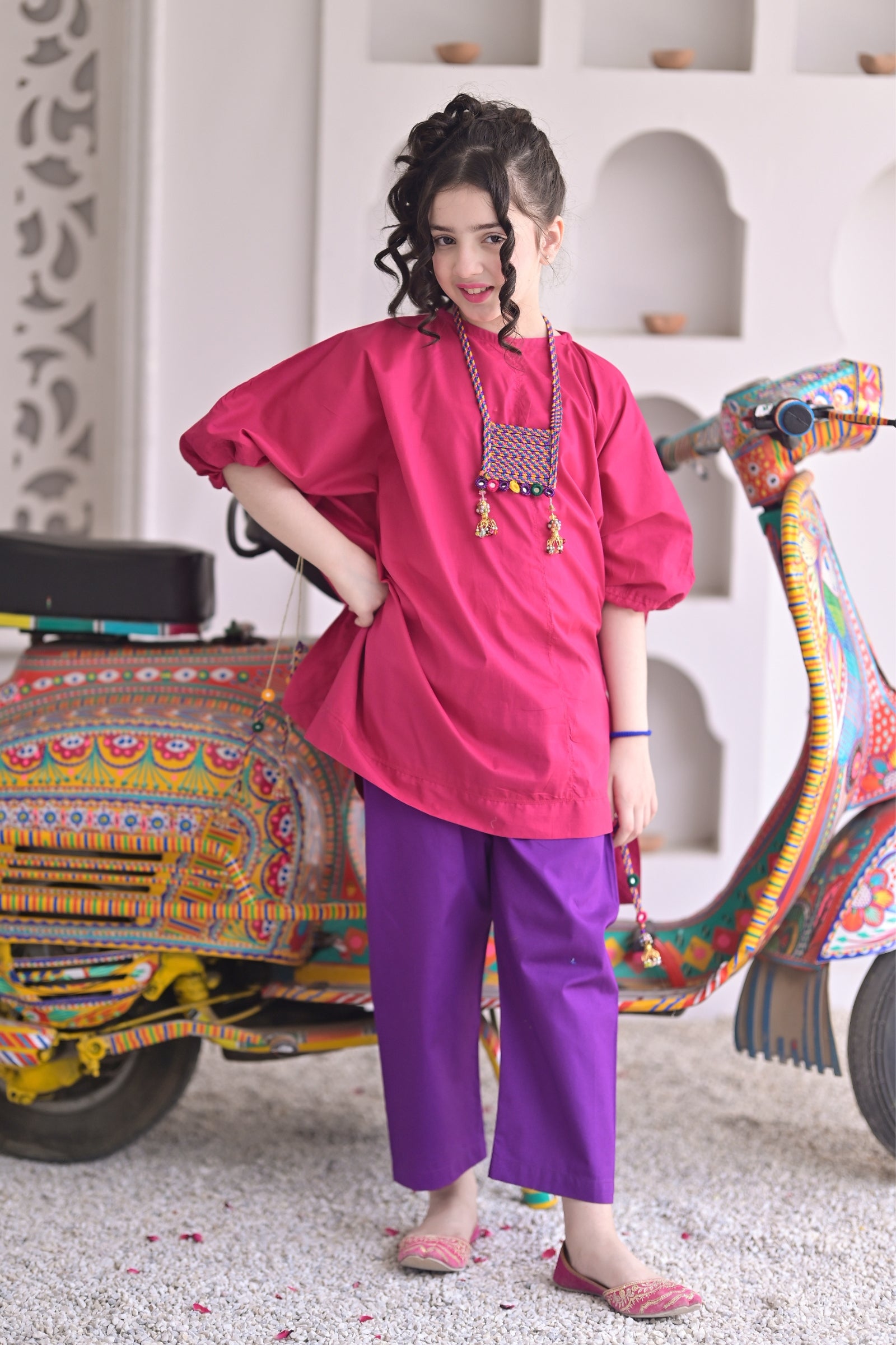 Full-length view of a girl posing in a pink cotton kaftan with tassels and matching purple pants.